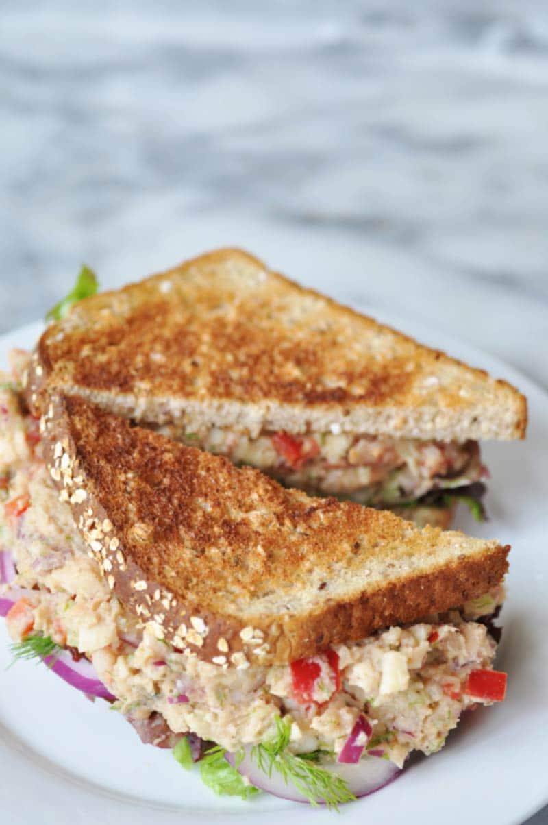 A tuna salad sandwich on toast, cut in half on a white plate.