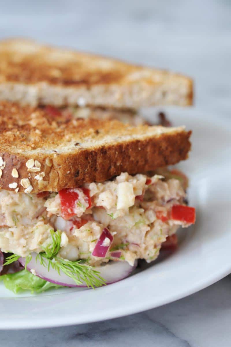 A close up picture of a tuna salad sandwich on toast on a white plate.