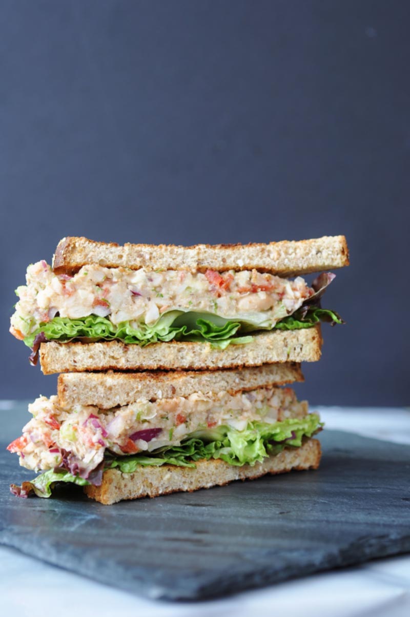A tuna salad sandwich on toast, cut in half and stacked on a slate board.