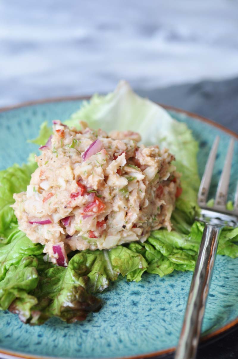 A scoop of tuna salad on a bed of greens on a blue plate with a silver fork on the edge of the plate.