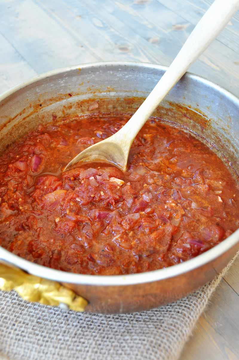 A copper pot with marinara sauce and a wood spoon in the pot