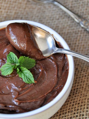 chocolate pudding in a white bowl with a silver spoon taking a scoop of it out of the bowl with a sprig of mint on top
