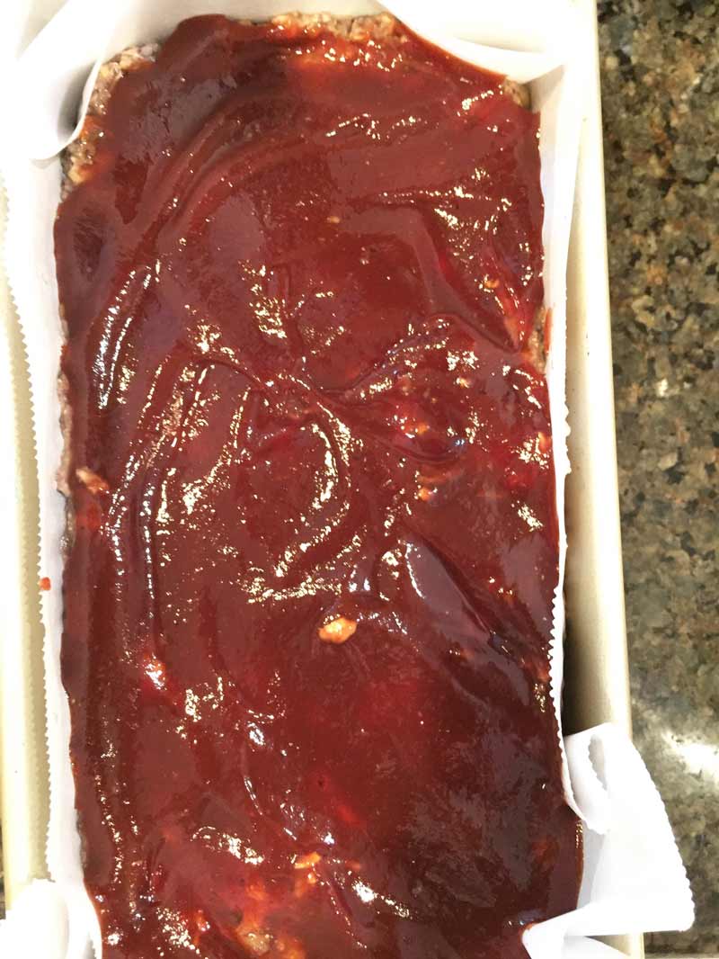 uncooked vegan meatloaf with BBQ sauce spread over the top in a bread pan with parchment paper