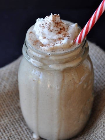 Gingerbread smoothie in a mason jar with a dollop of whipped cream and a red and white striped straw