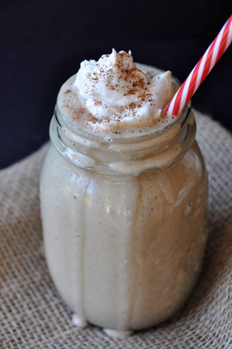 Gingerbread smoothie in a mason jar with a dollop of whipped cream and a red and white striped straw