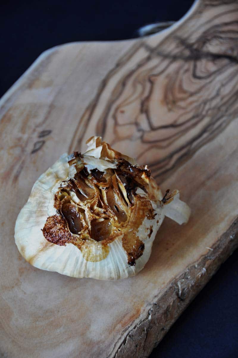 A bulb of roasted garlic on a wood board.