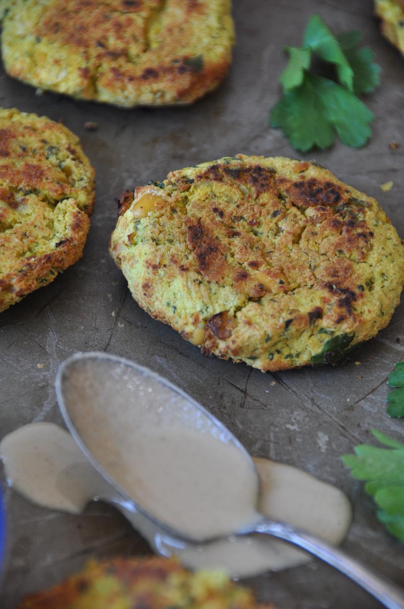 Crispy oven fried falafel on a metal tray with cilantro leaves and a spoon with tahini dripping off of it.