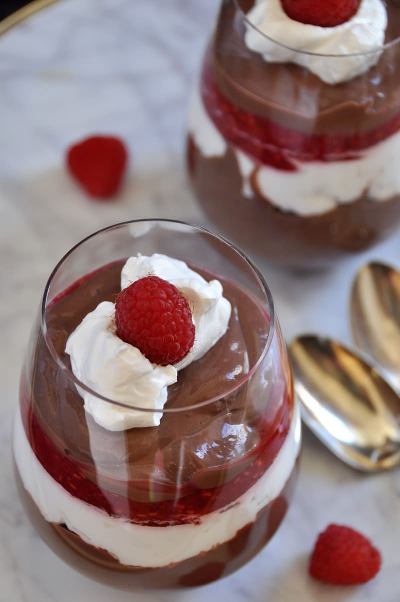 Two glasses of chocolate pudding with whipped cream and raspberries