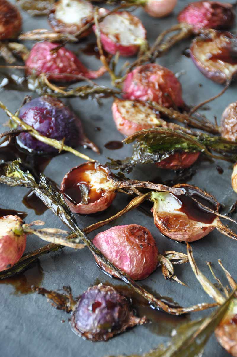 A slate board with roasted radishes and balsamic vinegar.