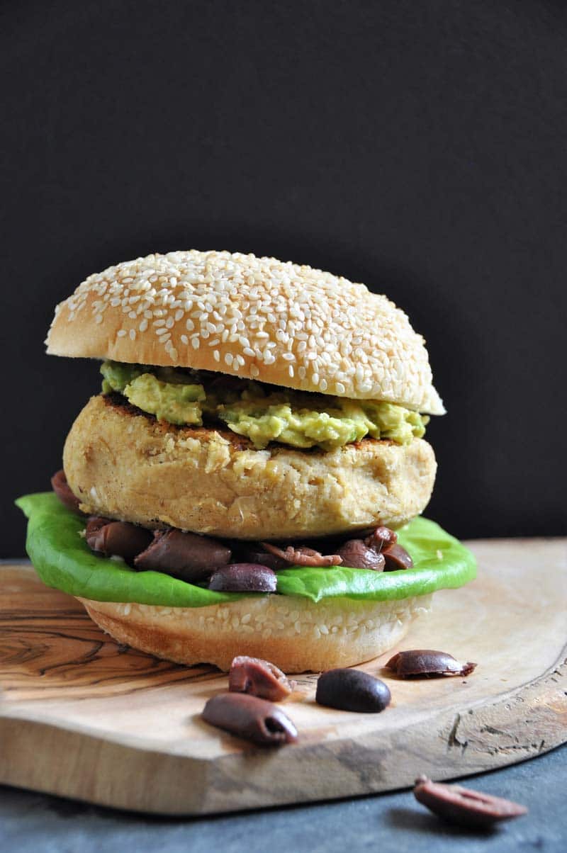 A Hummus Burger on a wood board with olives falling out of it.