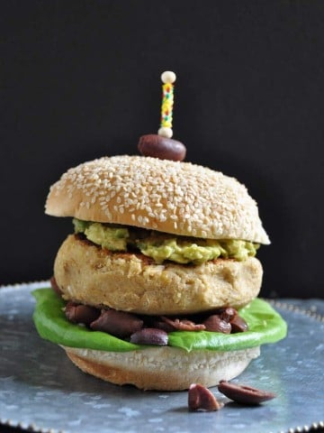 A Hummus burger on a silver plate with an olive stuck on the top with a toothpick