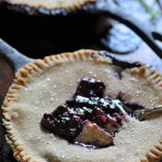 A blueberry pie in an iron skillet with a fork taking a piece out of the center of the pie.