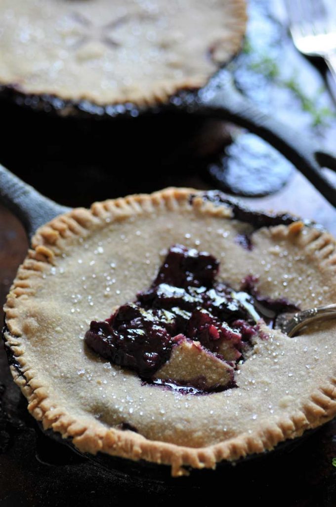 A blueberry pie in an iron skillet with a fork taking a piece out of the center of the pie.