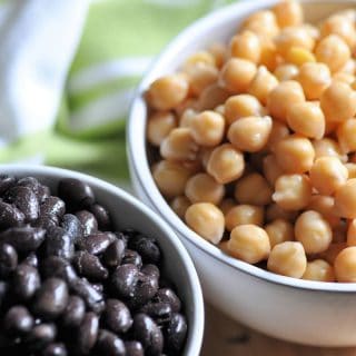 2 white bowls, one is filled with cooked black beans and one with cooked garbanzo beans.