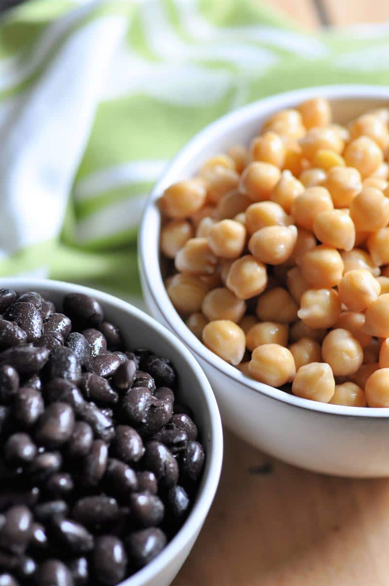 2 white bowls, one filled with black beans and the other with garbanzo beans. 