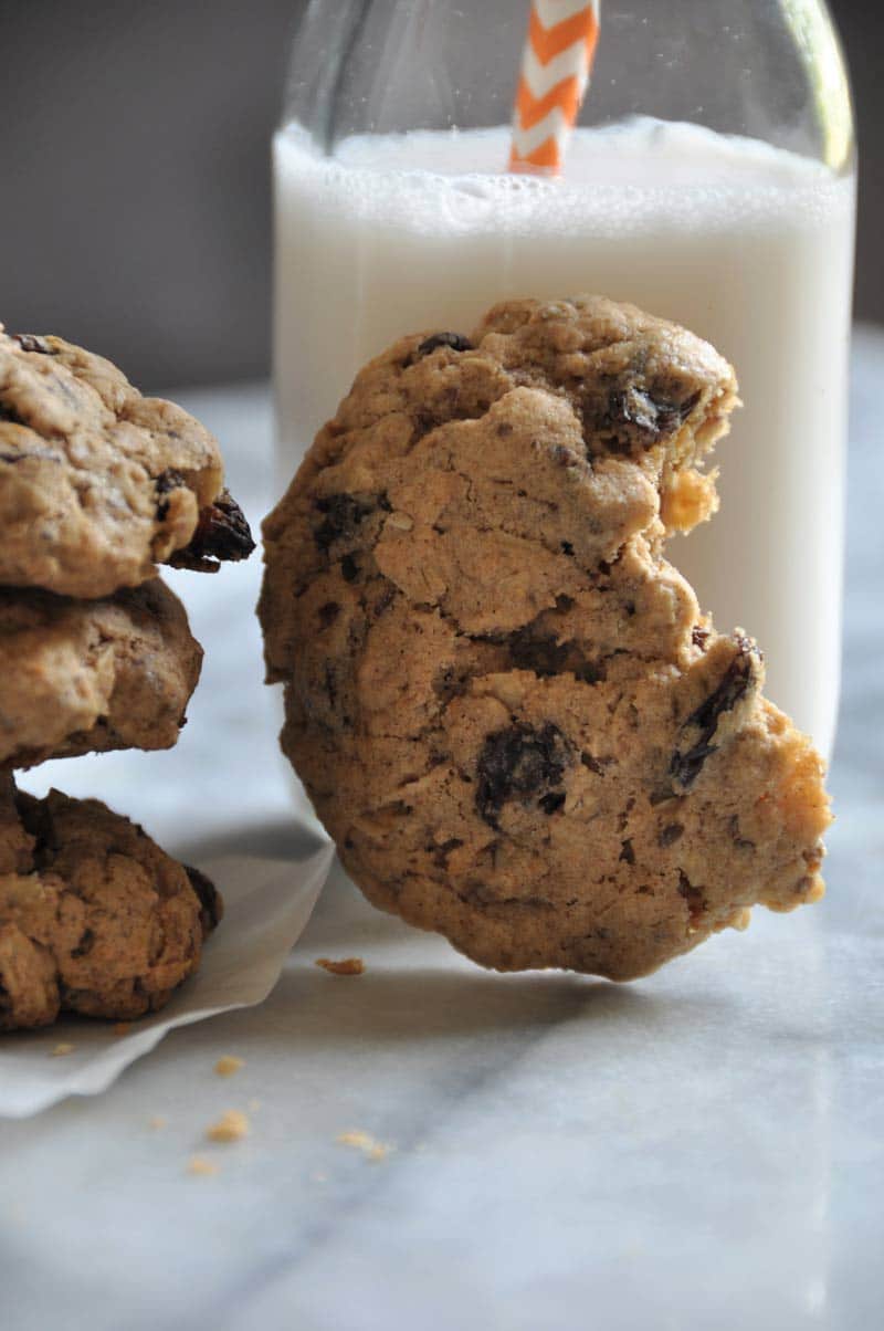 An oatmeal raisin cookie with a bite out of it, leaning on a glass of milk. 