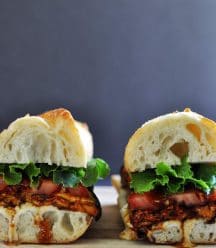 2 halves of an ELT (eggplant, lettuce & tomato) sandwich on a wood board.