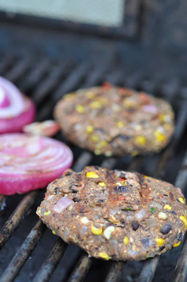 Black bean veggie burgers cooking on a grill next to sliced red onions.