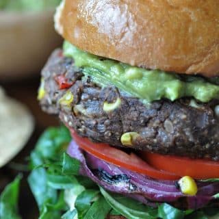 A black bean and veggie burger with corn, tomatoes, lettuce, and guacamole on top.