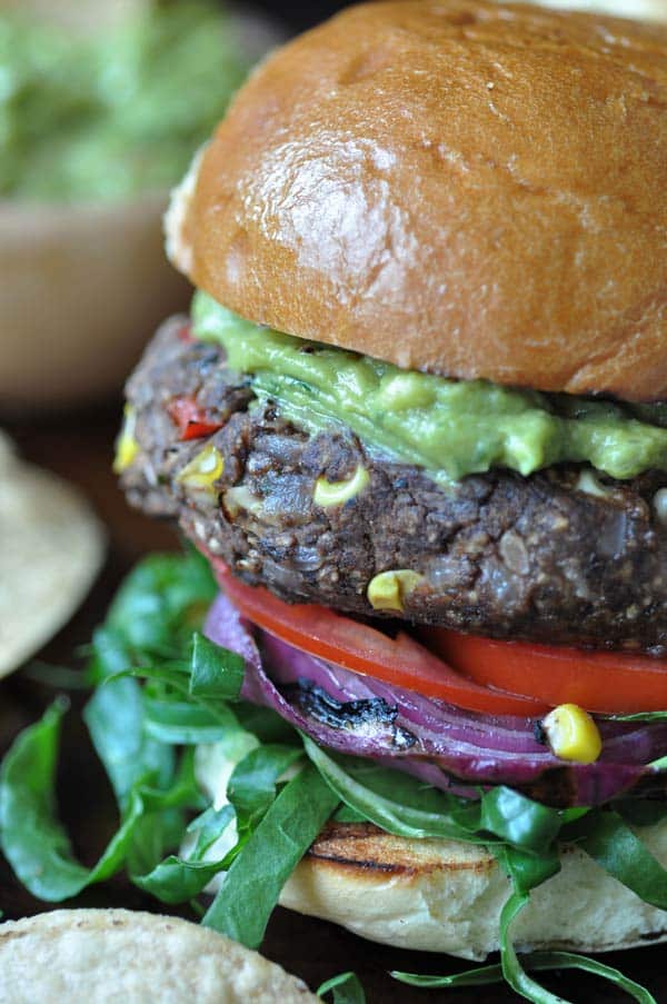 A black bean and veggie burger with corn, tomatoes, lettuce, and guacamole on top.