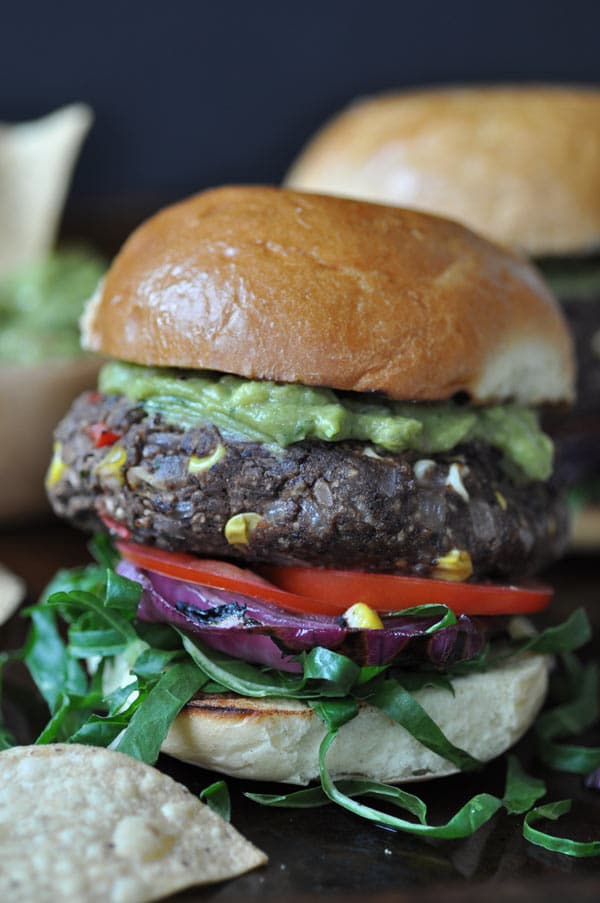 A black bean and veggie burger with corn, tomatoes, lettuce, and guacamole on top. 