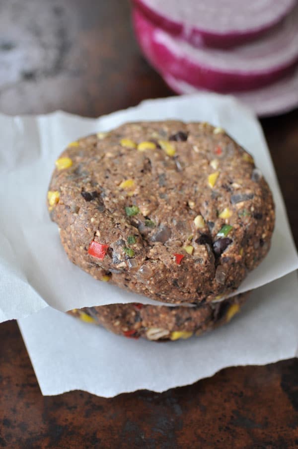 Uncooked black bean veggie burgers stacked between squares of parchment paper.