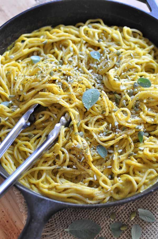  Creamy Pumpkin Sage Sauce with Spaghetti in an iron skillet with silver tongs in the pan and cracked pepper and sage leaves sprinkled on top