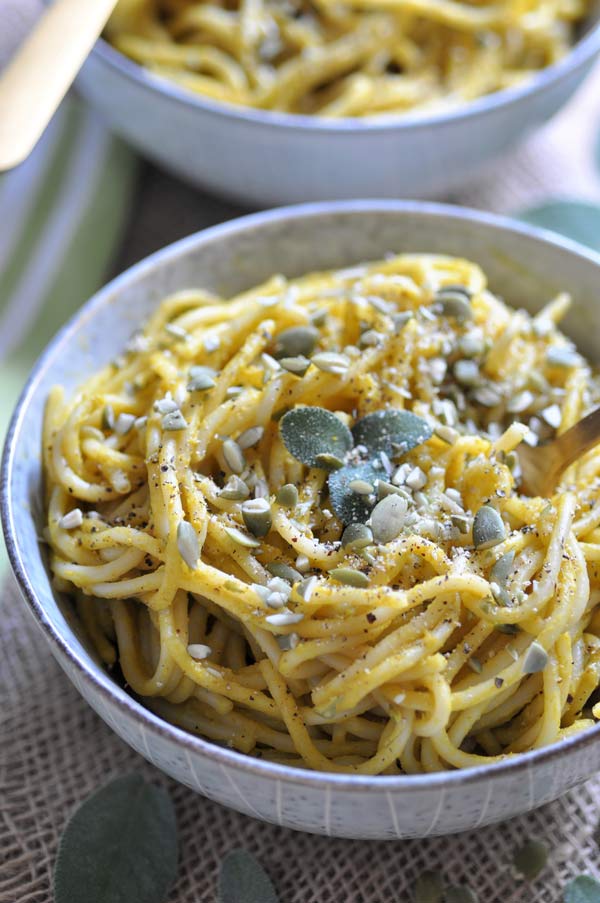 Spaghetti with a fresh and creamy pumpkin sage sauce in a grey bowl with pepitas and sage leaves on top and a bowl in the background