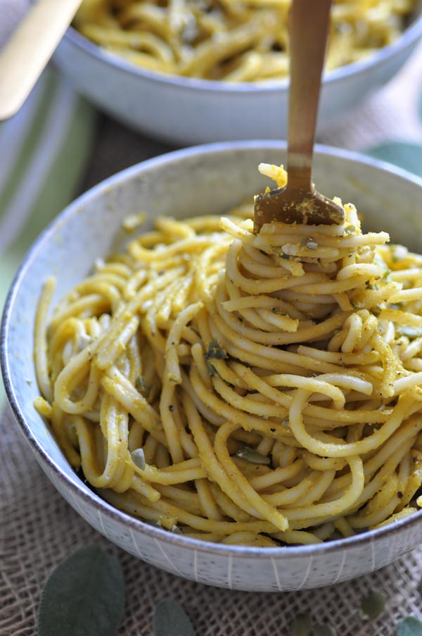 A creamy pumpkin sage cream sauce smothered over spaghetti in a grey bowl with a gold fork winding up the spaghetti in the center of the bowl