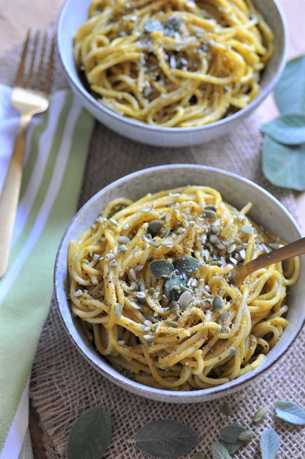 Pumpkin sage cream sauce smothered over spaghetti in a white bowl, sprinkled with pepitas and sage leaves. 