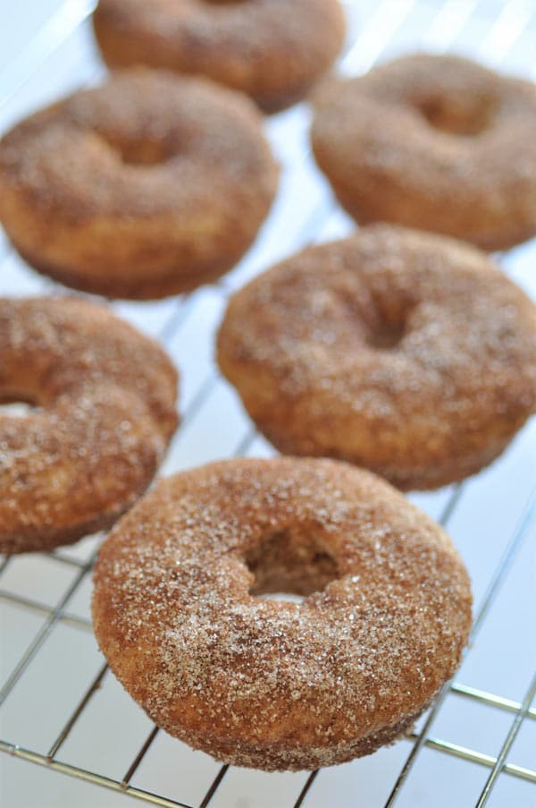 Vegan baked apple cider doughnuts covered in sugar on a wire rack