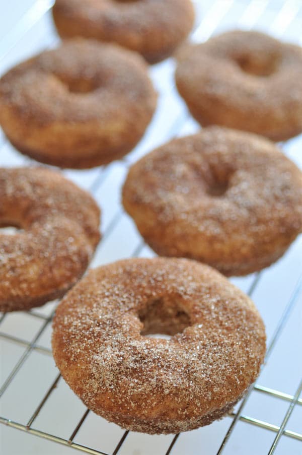 Vegan baked apple cider doughnuts covered in sugar on a wire rack