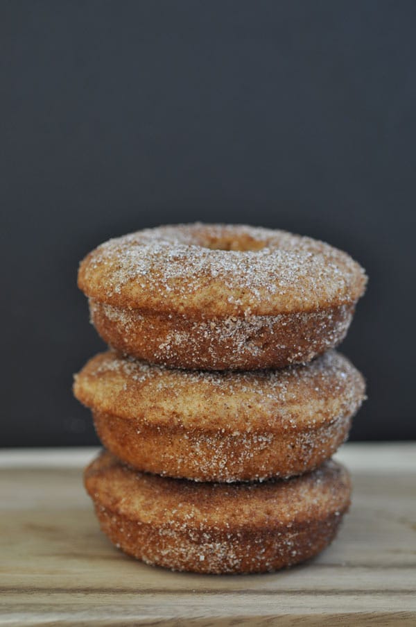 Three baked vegan apple cider doughnuts stacked on a wood board