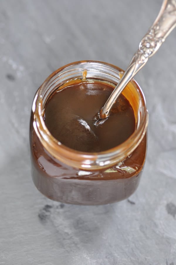 Vegan Salted Caramel Sauce in a clear jar with a silver spoon in it on a slate surface