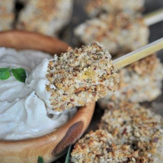 A skewer with a crusted almond tofu bite being dipped into lemon ginger dip in a wood bowl.