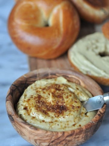 Vegan pumpkin spread in a wooden bowl with bagels on a wood board.