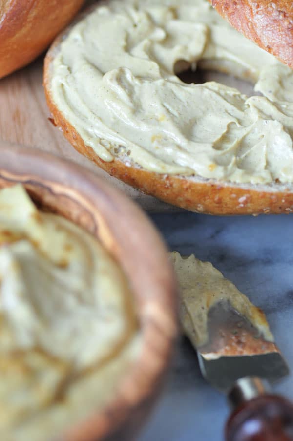 Creamy vegan pumpkin spread on a bagel with a blurred shot of the spread in a wood bowl. 