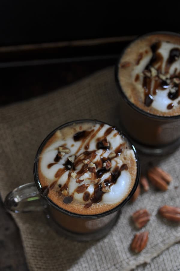 2 Maple Pecan Lattes in clear glass mugs on a burlap cloth with pecans scattered on it