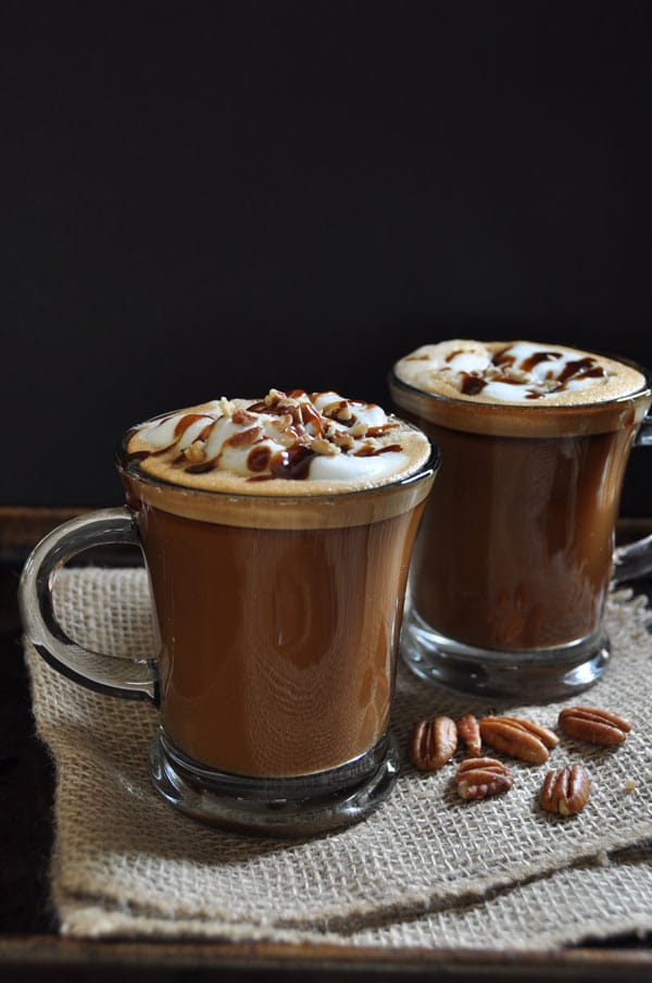 2 clear glass mugs of Maple Pecan Lattes on burlap with pecans scattered and a black background
