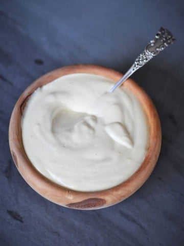 Vegan cheese sauce in a wood bowl with a silver spoon in the sauce.