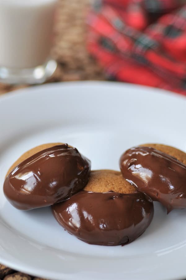 Three chocolate dipped ginger cookies overlapping on a white plate.
