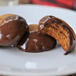Three Ginger Cookies dipped in chocolate, one with a bite out of it, on a white plate