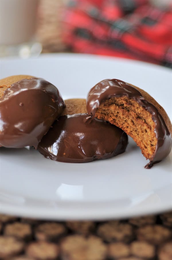 Three Ginger Cookies dipped in chocolate, one with a bite out of it, on a white plate