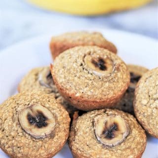 A stack of banana muffins on a white plate with bananas in the background