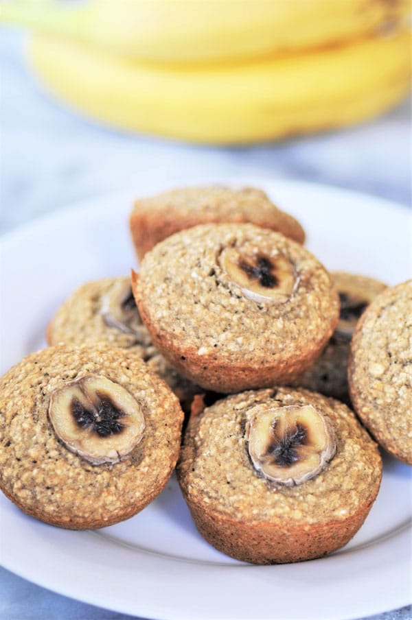 A stack of banana muffins on a white plate with bananas in the background