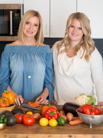 A picture of Linda and Alex standing next to a wooden table with lots of colorful vegetables, promoting Veganosity's first cookbook; Great Vegan BBQ Without a Grill.