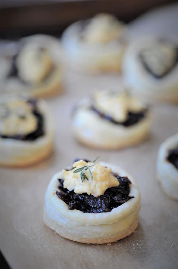 A close up of an onion confit tartlet with vegan ricotta and thyme on parchment paper.