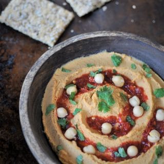 A wood bowl of spicy peanut chili hummus with chili sauce, cilantro, and whole chickpeas