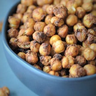 Spicy roasted chickpeas in a black bowl on a black piece of slate with chickpeas spilling over.