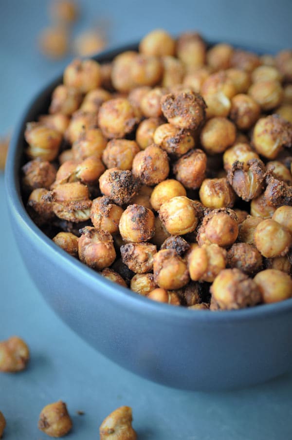 Spicy roasted chickpeas in a black bowl on a black piece of slate with chickpeas spilling over. 